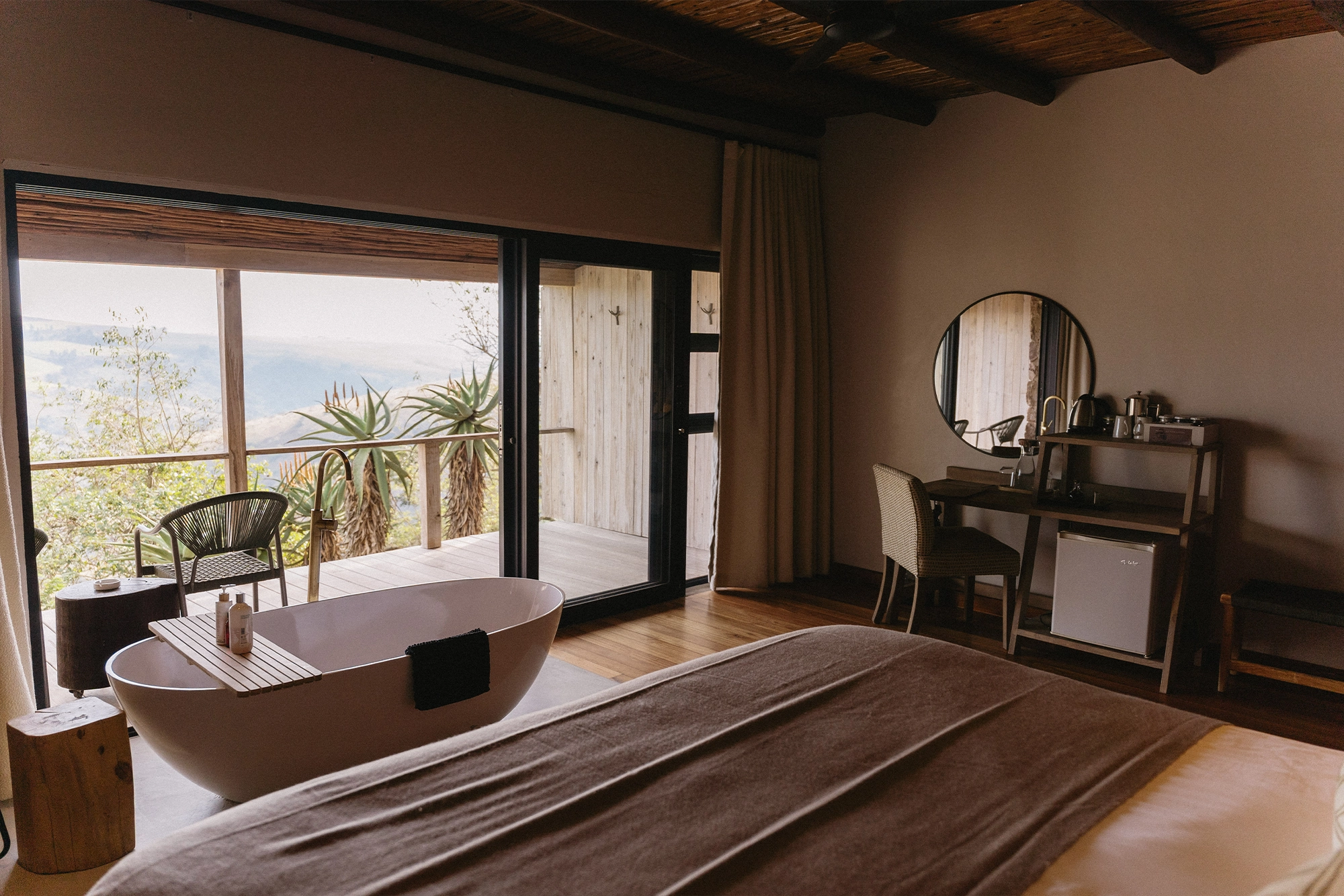 This photograph shows the bed in Serenegti. There is modern wooden slatting on the wall and large lamps on the bedside tables.